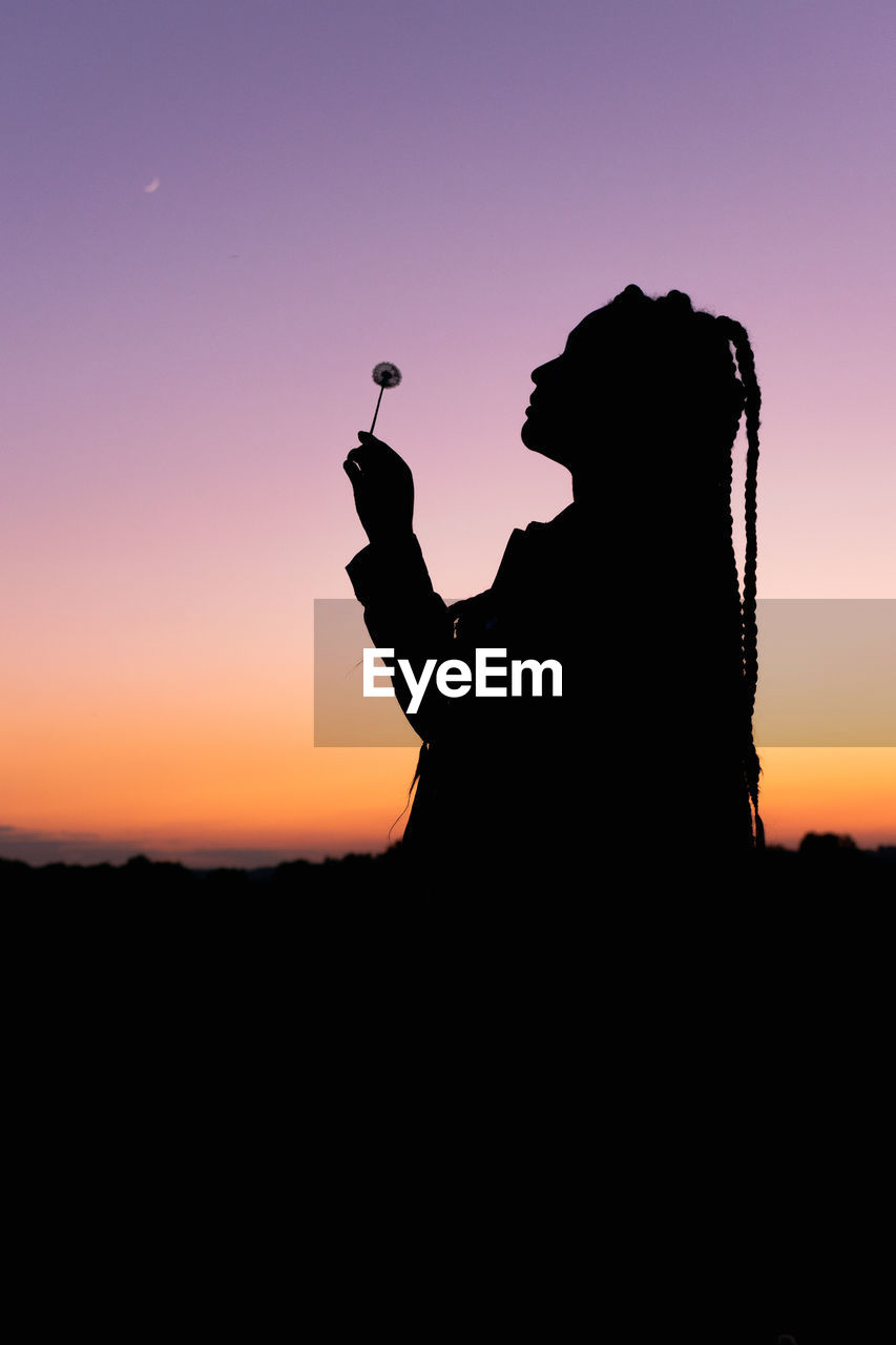 Silhouette woman holding lollipop standing against sky during sunset