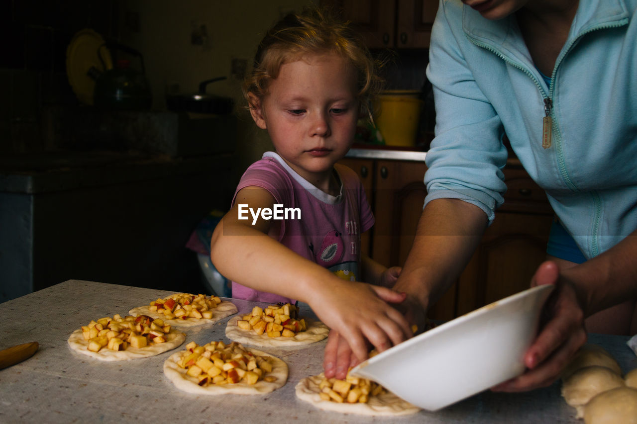 A girl prepares pies with apples in the kitchen