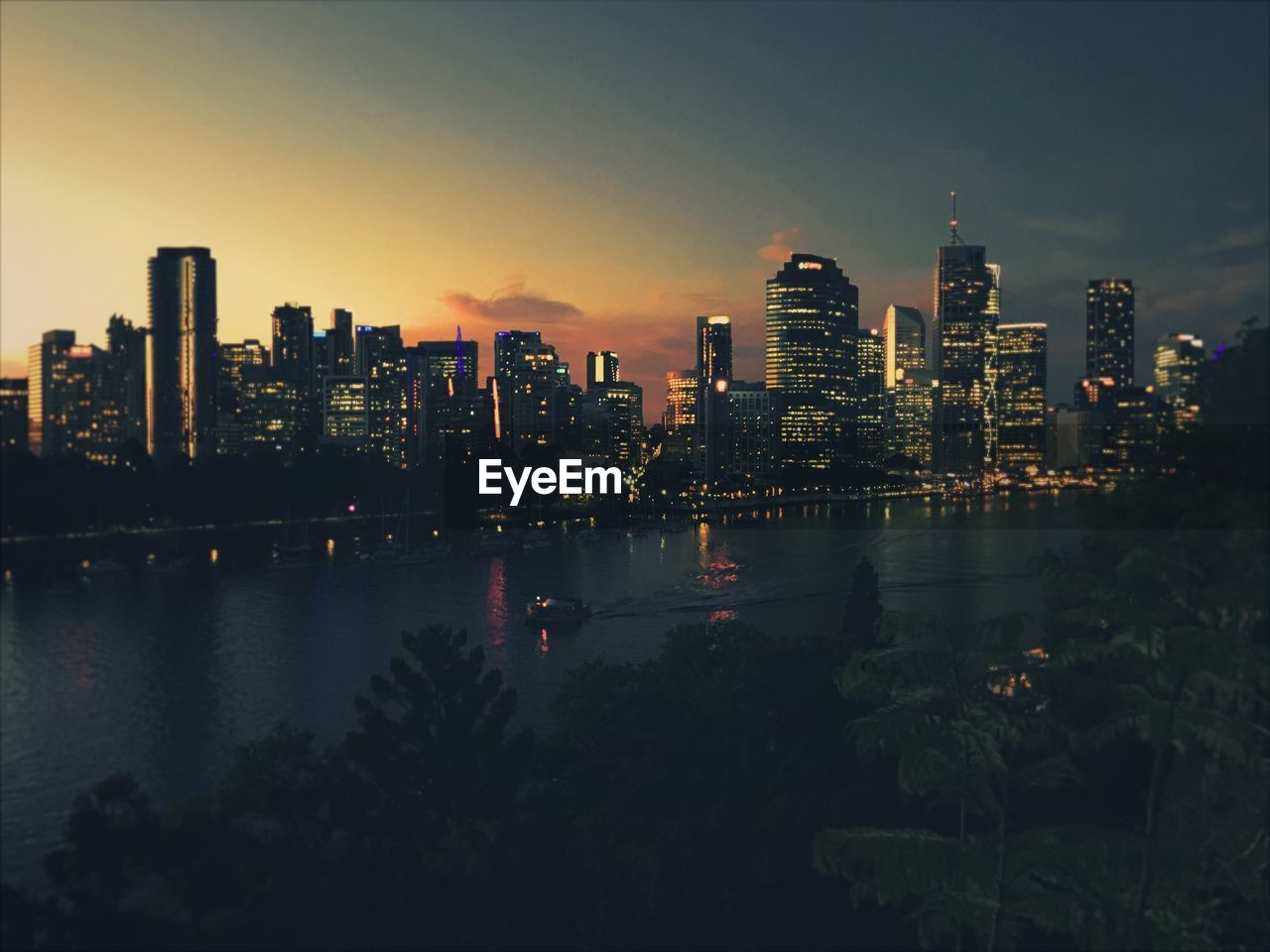 Illuminated buildings by river against sky in city