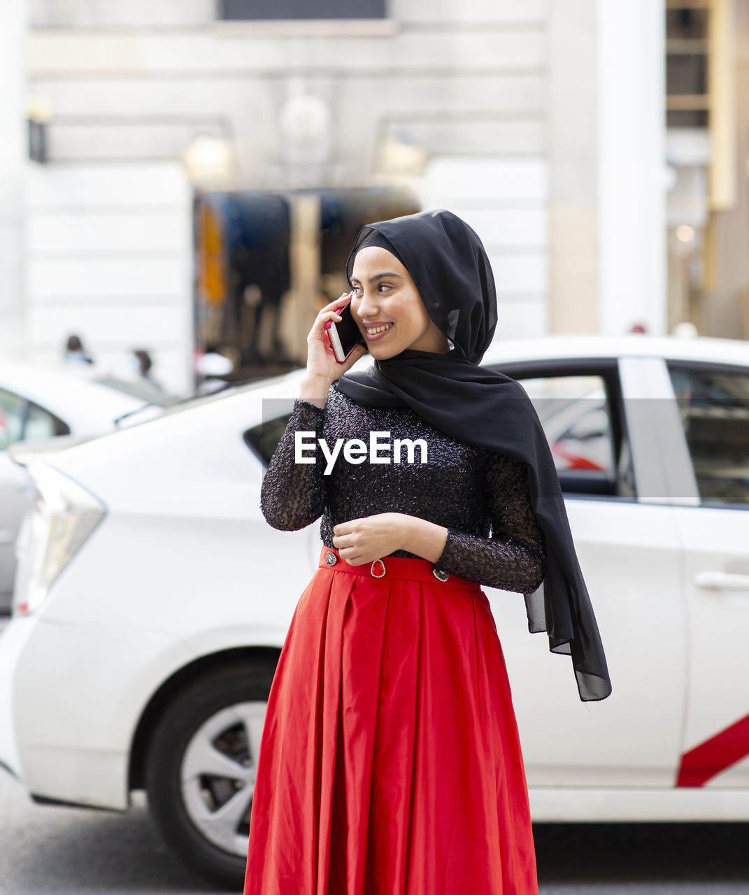 Portrait of young beautiful woman wearing black hijab talking on smart phone in middle of street
