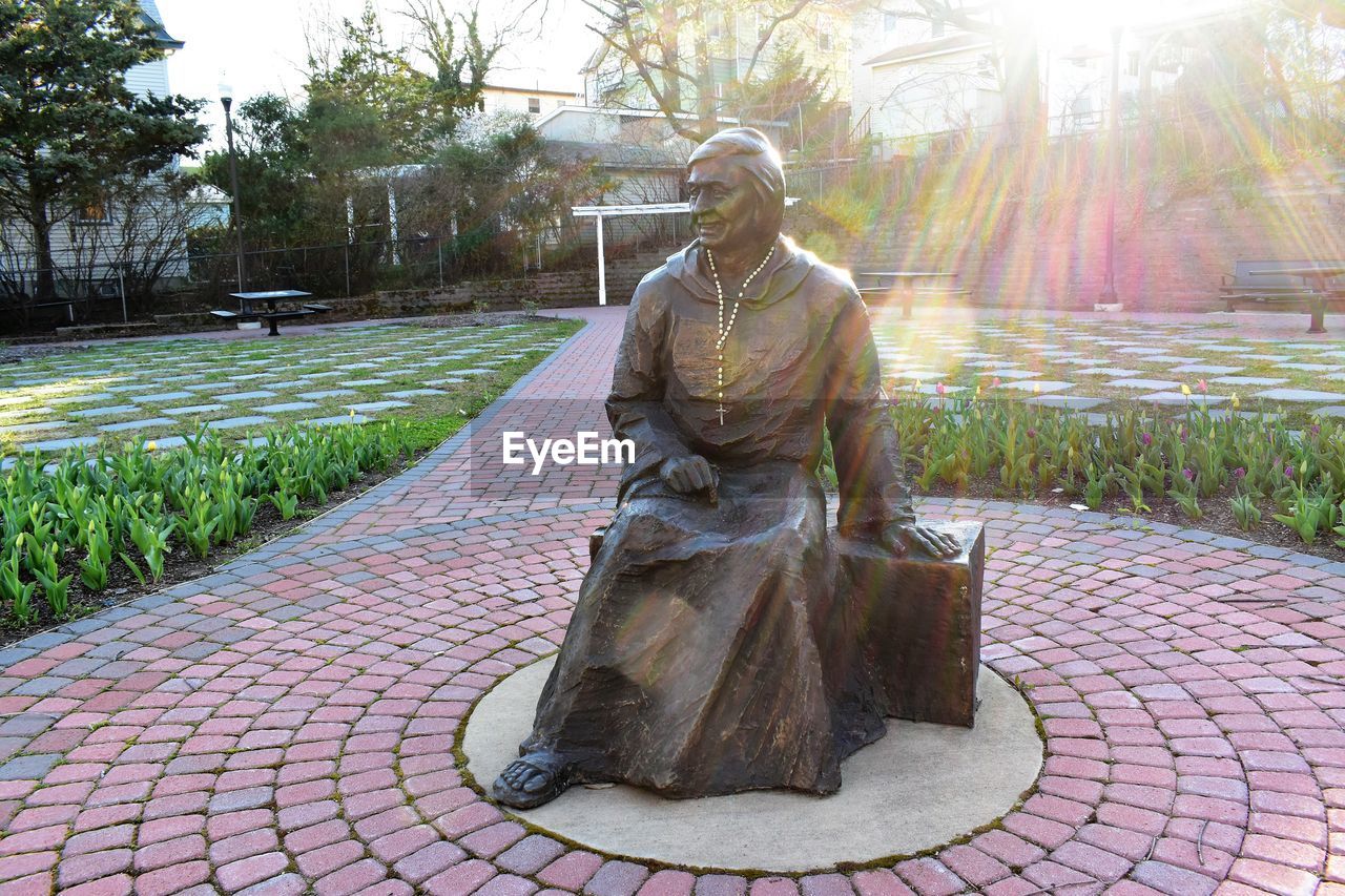 statue, sculpture, plant, nature, tree, bronze sculpture, monument, human representation, representation, day, footpath, sunlight, park, architecture, person, park - man made space, art, outdoors, creativity, religion, sky, male likeness, garden, city, cobblestone, lens flare, craft, adult, travel destinations