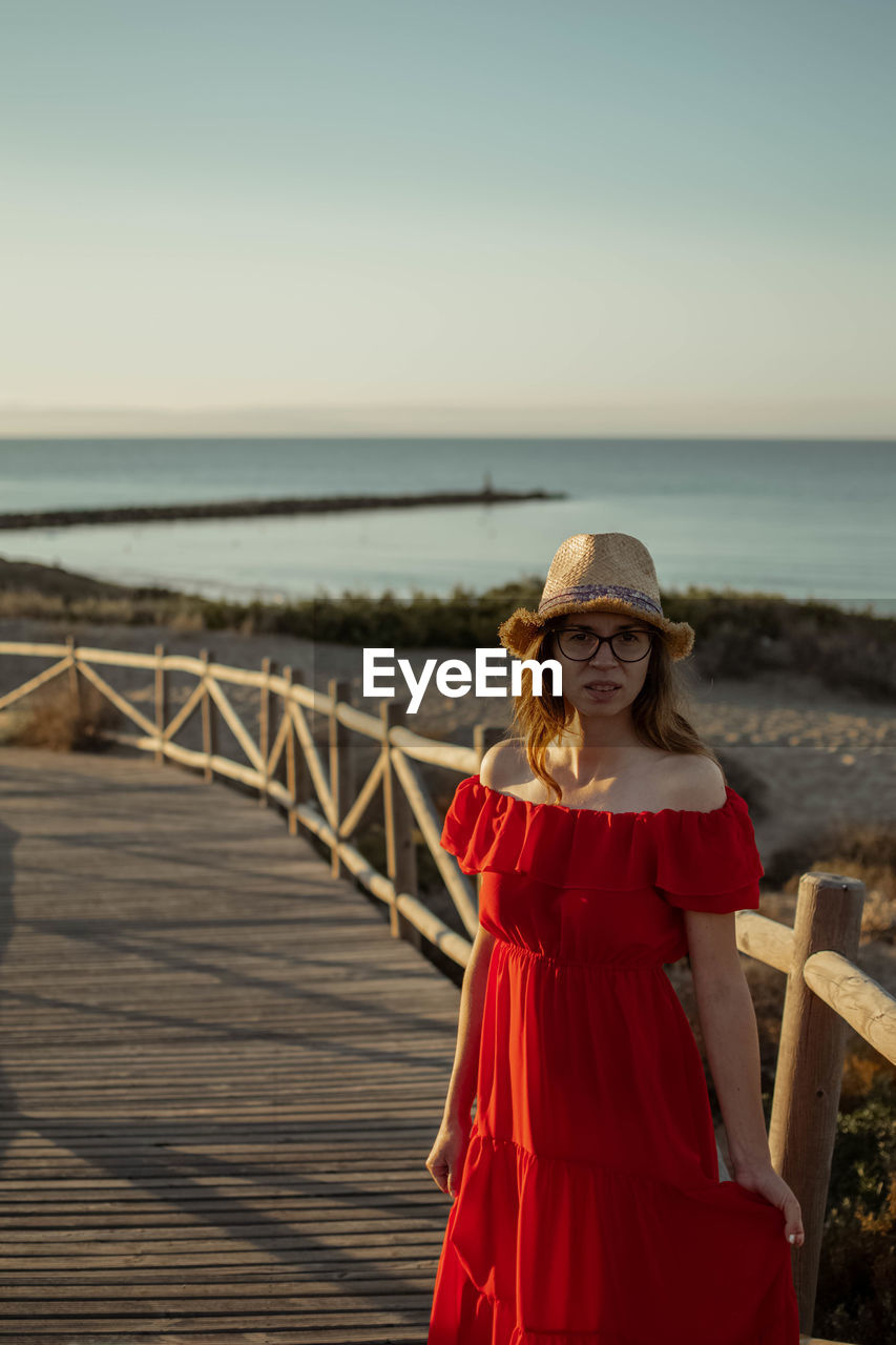 Portrait of young woman standing at beach against sky