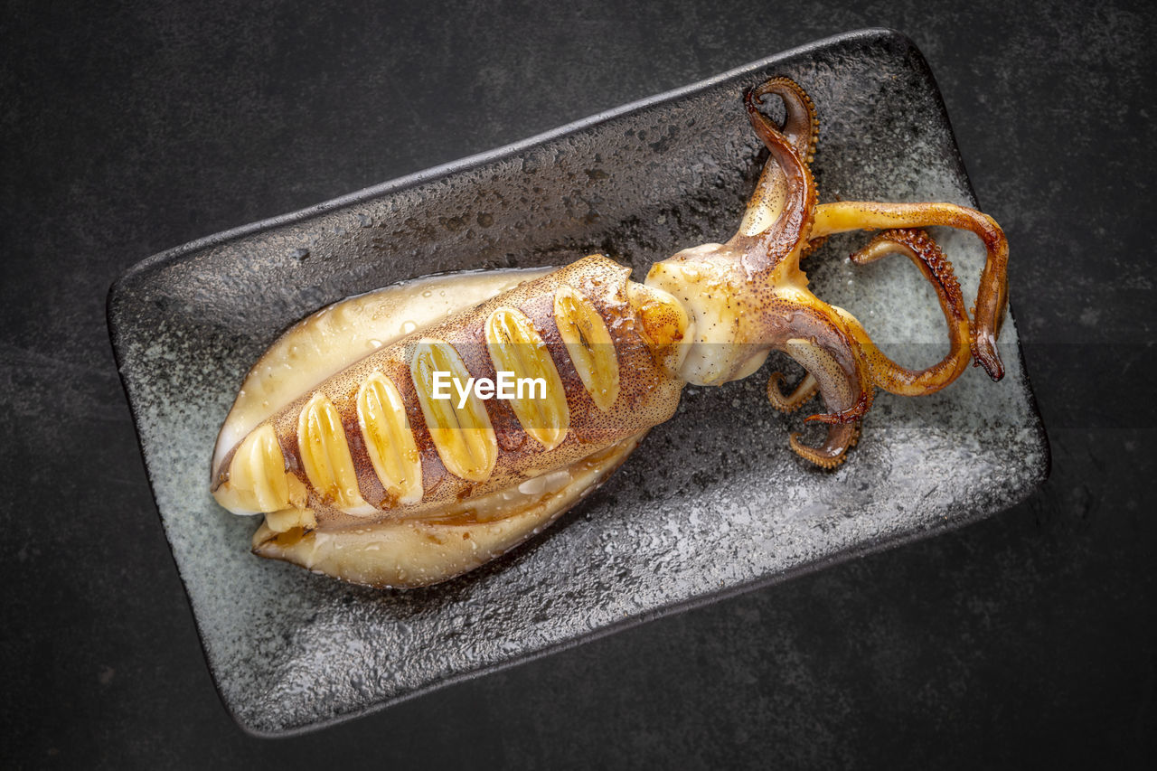 Fried whole squid in ceramic plate on dark tone texture background, top view