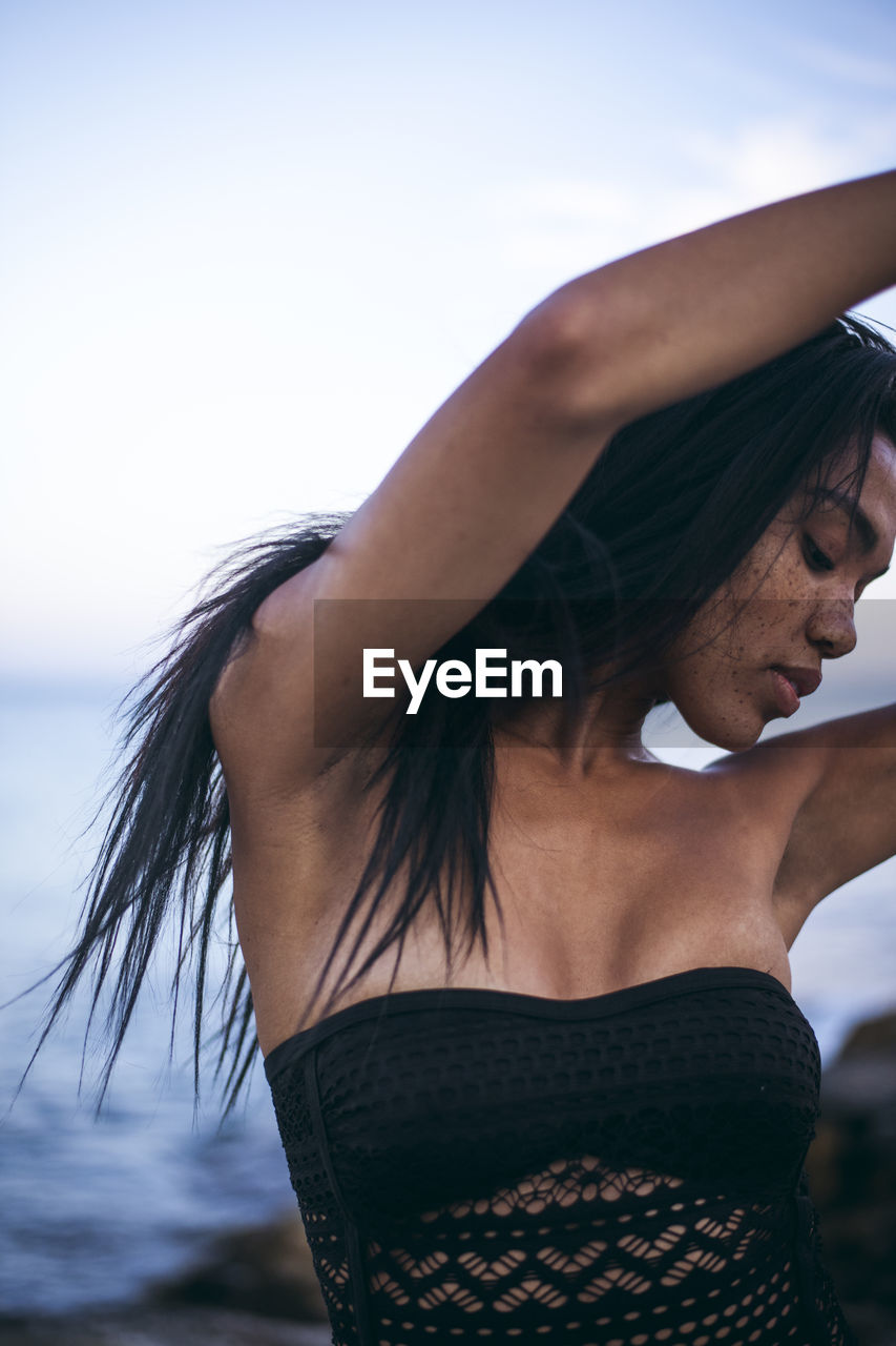 Black multiracial woman lifestyle portrait by the ocean in a swimsuit