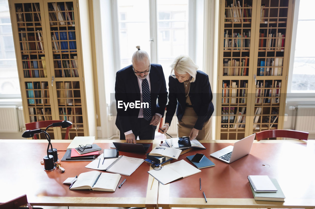 High angle view of senior lawyers using technologies at table in library