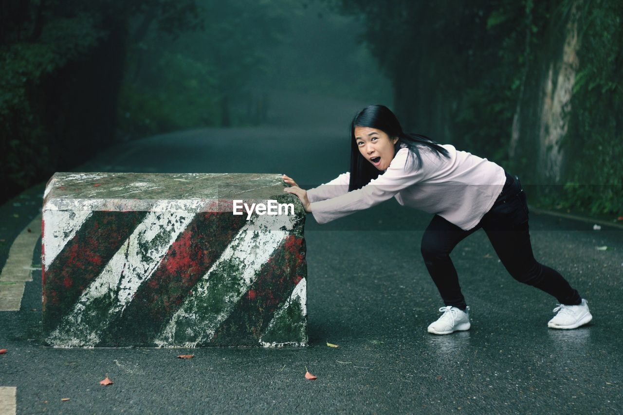 Full length portrait of young woman pushing stone on road