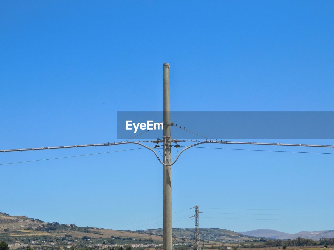 Low angle view of electricity pylon against clear blue sky