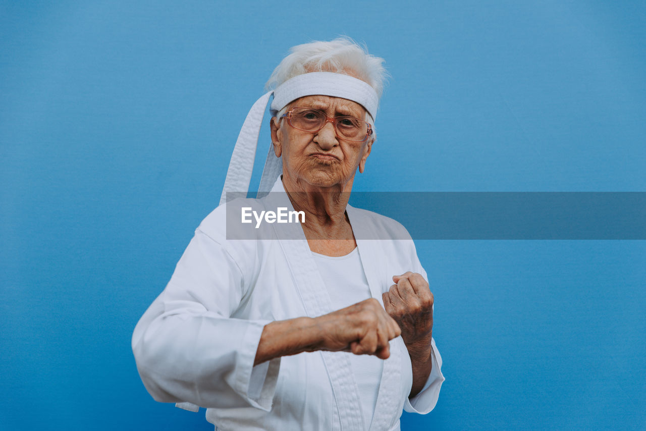 Portrait of senior woman doing karate against blue background