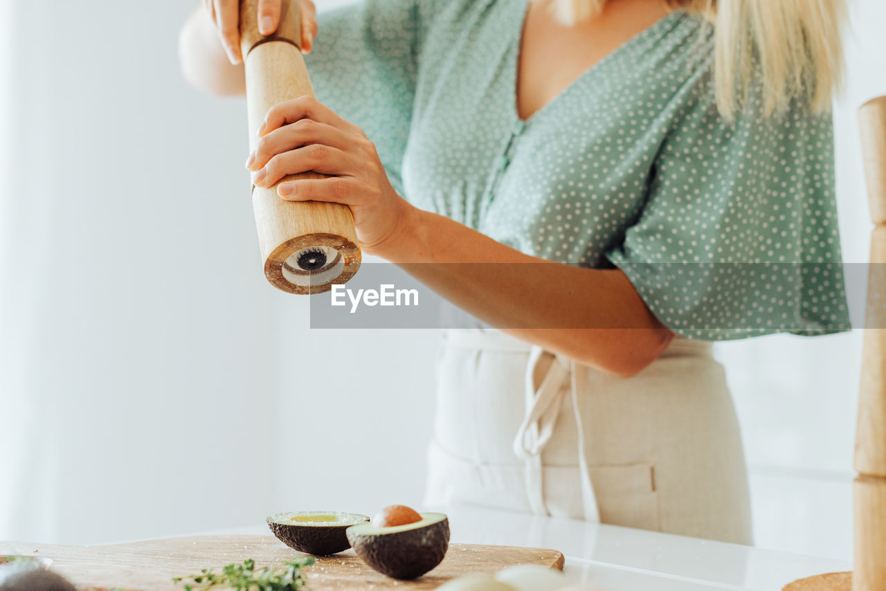 Midsection of a woman seasoning avocado with a manual spice grinder