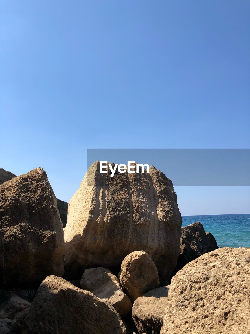 ROCKS ON SHORE AGAINST CLEAR BLUE SKY