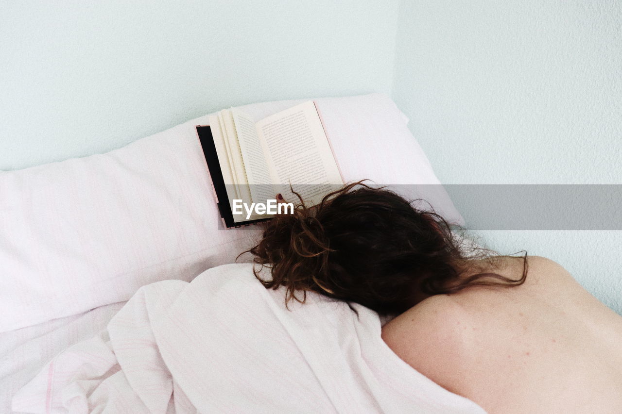 High angle view of topless teenager lying on bed by book at home