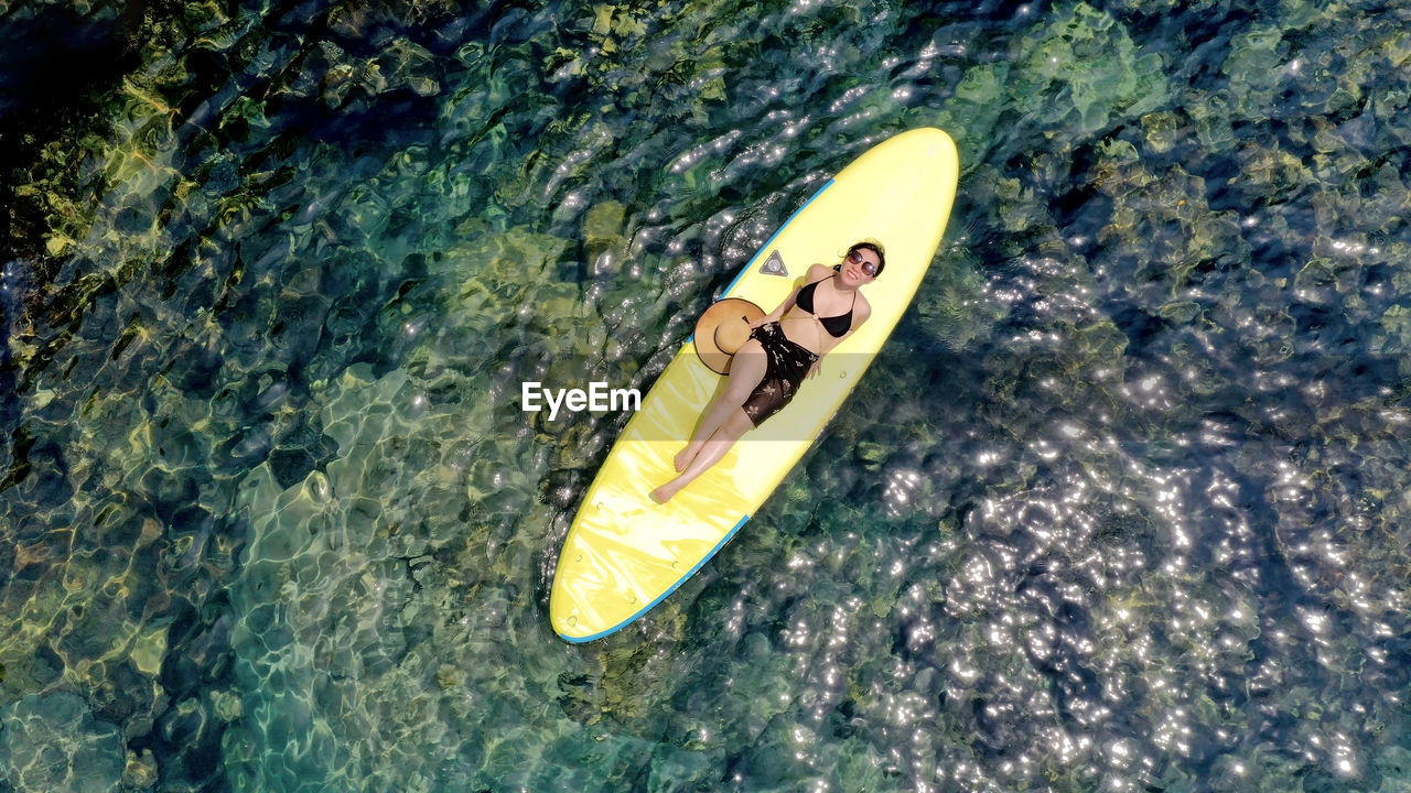 High angle view of a young woman floating on a surfboard in the middle of the sea