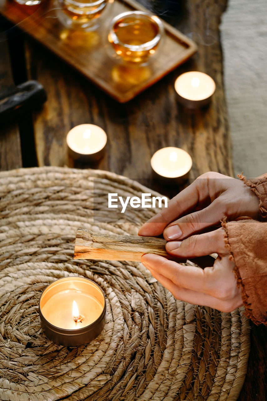 Woman hands burning palo santo, before ritual on the table with candles and green plants. smoke of