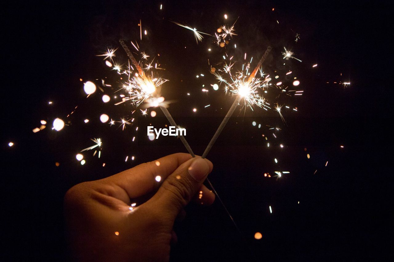 Cropped hand of person holding illuminated sparklers at night