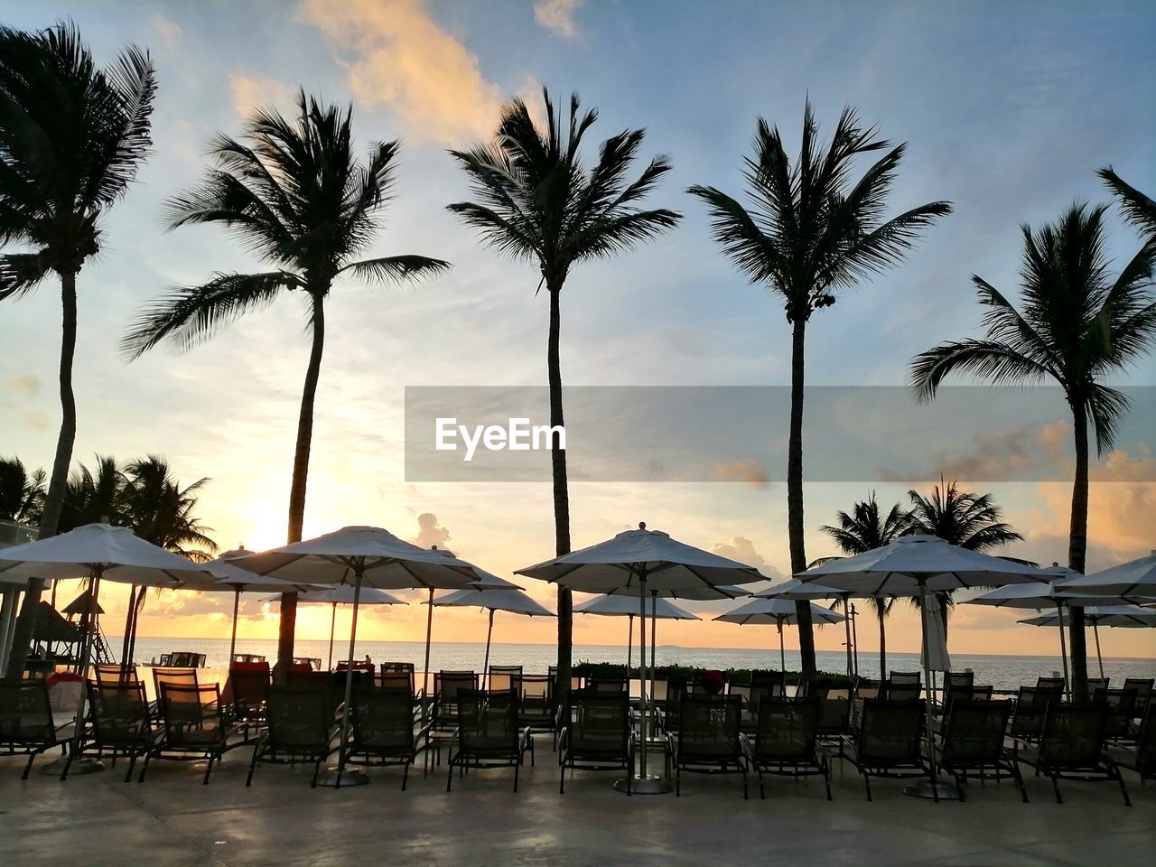 LOUNGE CHAIRS AND TABLES AT BEACH DURING SUNSET