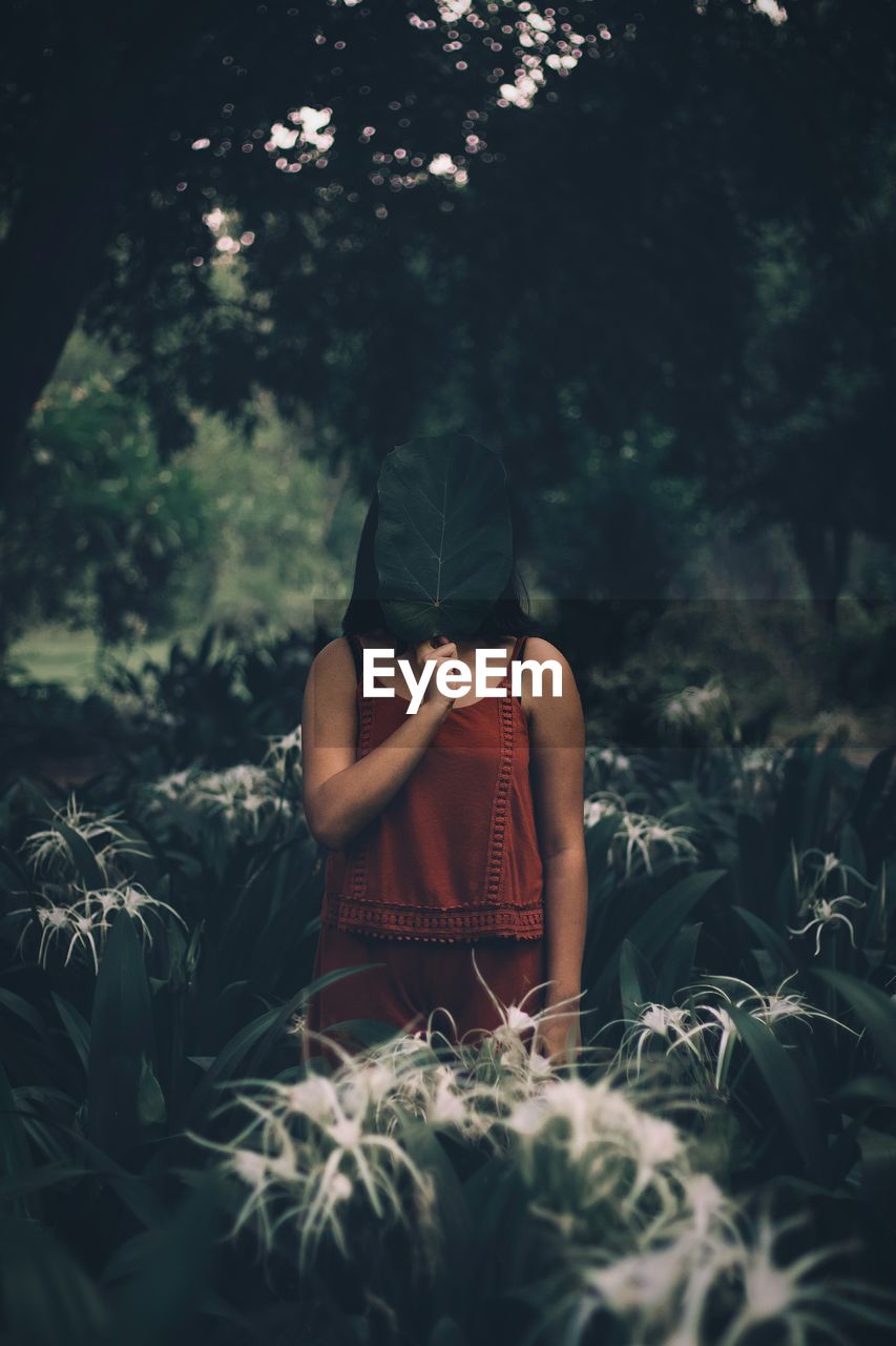 Woman covering face while standing in forest