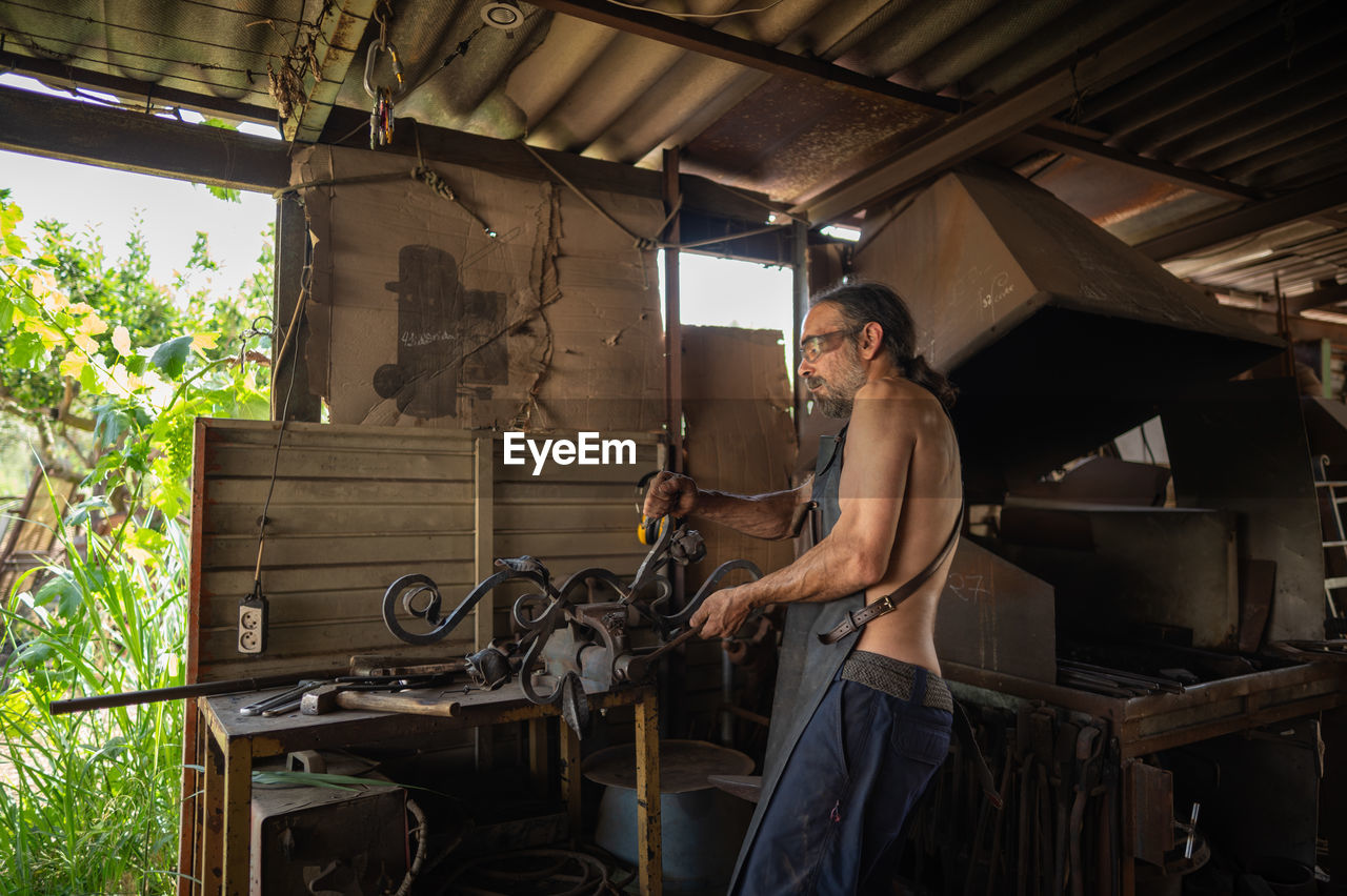 Side view of blacksmith shaping a decorative grille in his workshop. blacksmith concept.