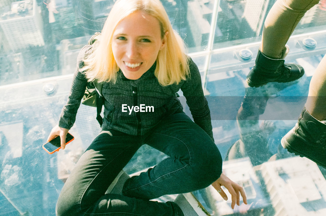 Portrait of woman sitting on glass at skydeck chicago in willis tower