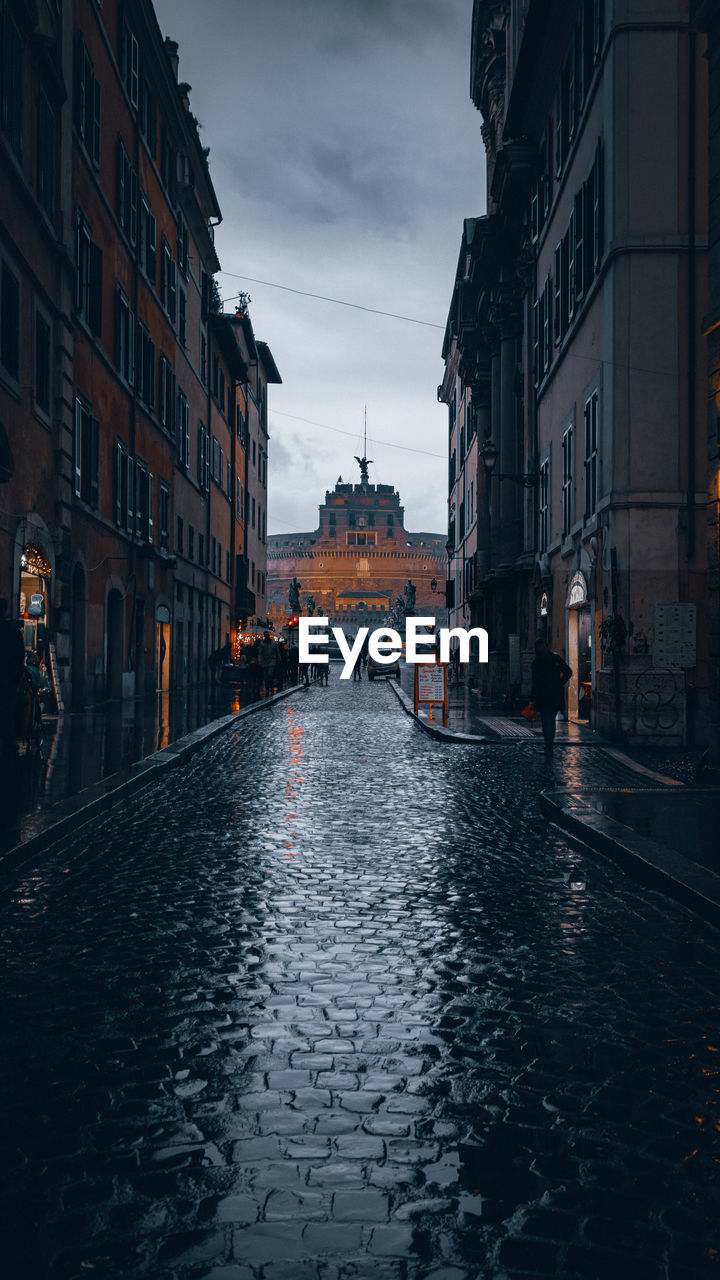 Wet cobblestones road amidst buildings in city