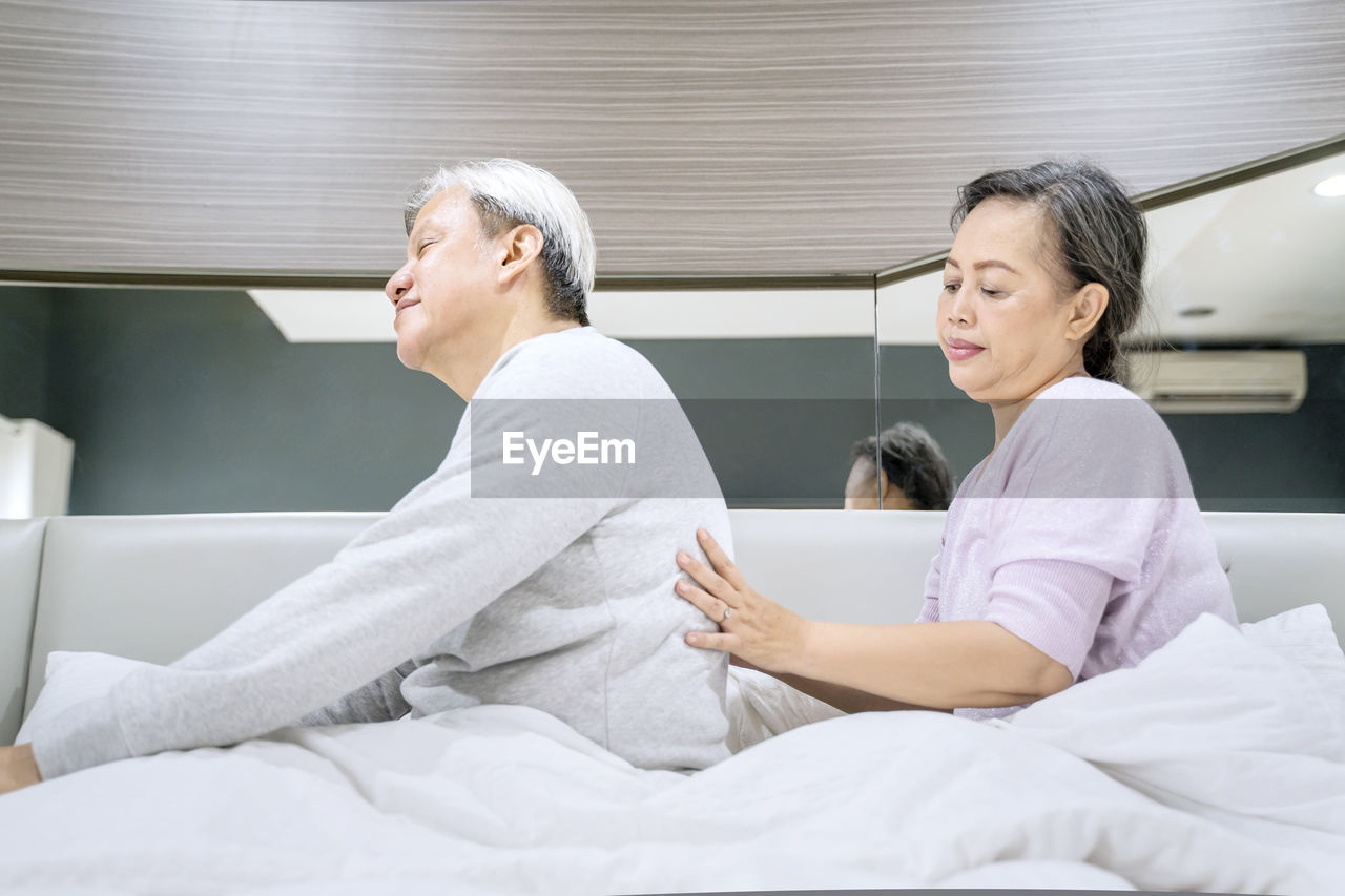 Side view of woman massaging man back on bed