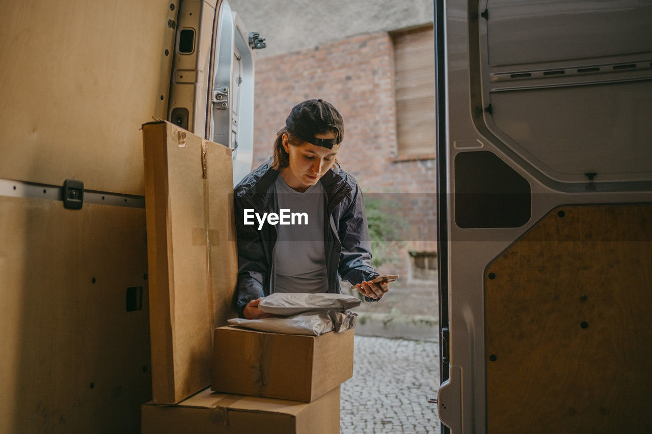 Female courier delivery person taking inventory of packages in van trunk