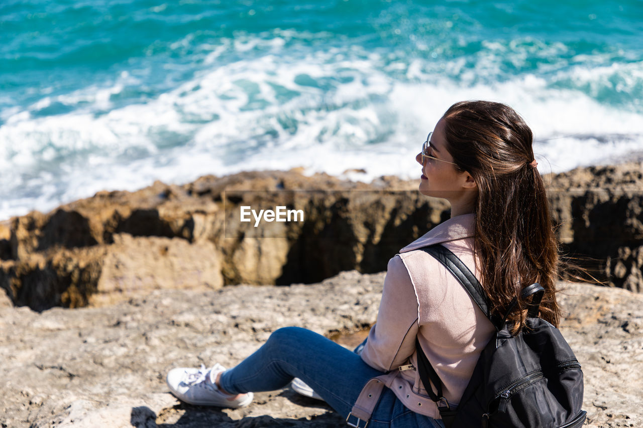 Rear view of woman sitting on rock at beach