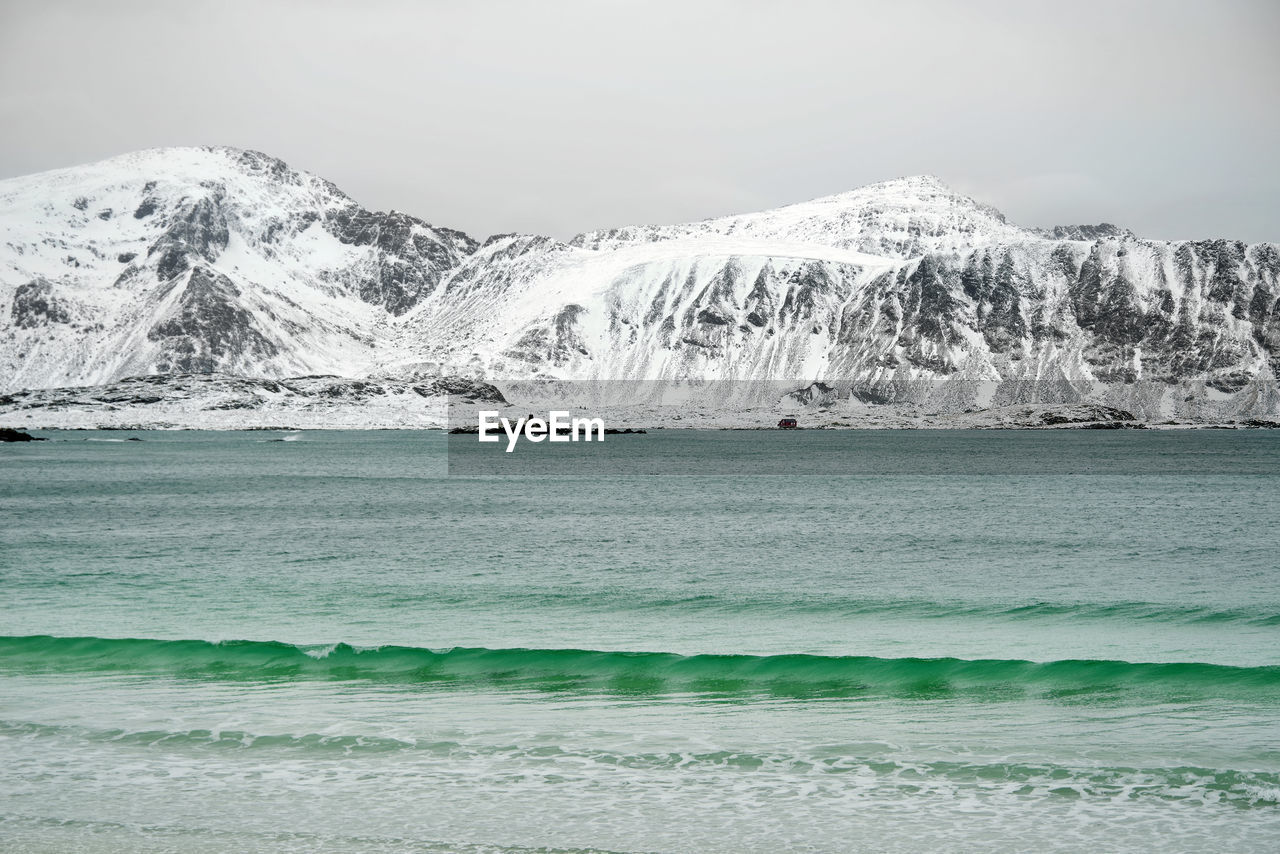 Scenic view of sea by mountain against sky