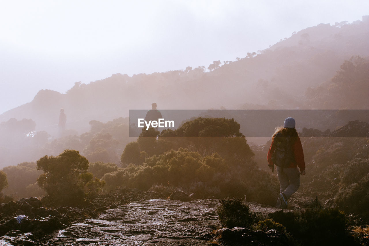 Rear view of people walking on mountain against sky