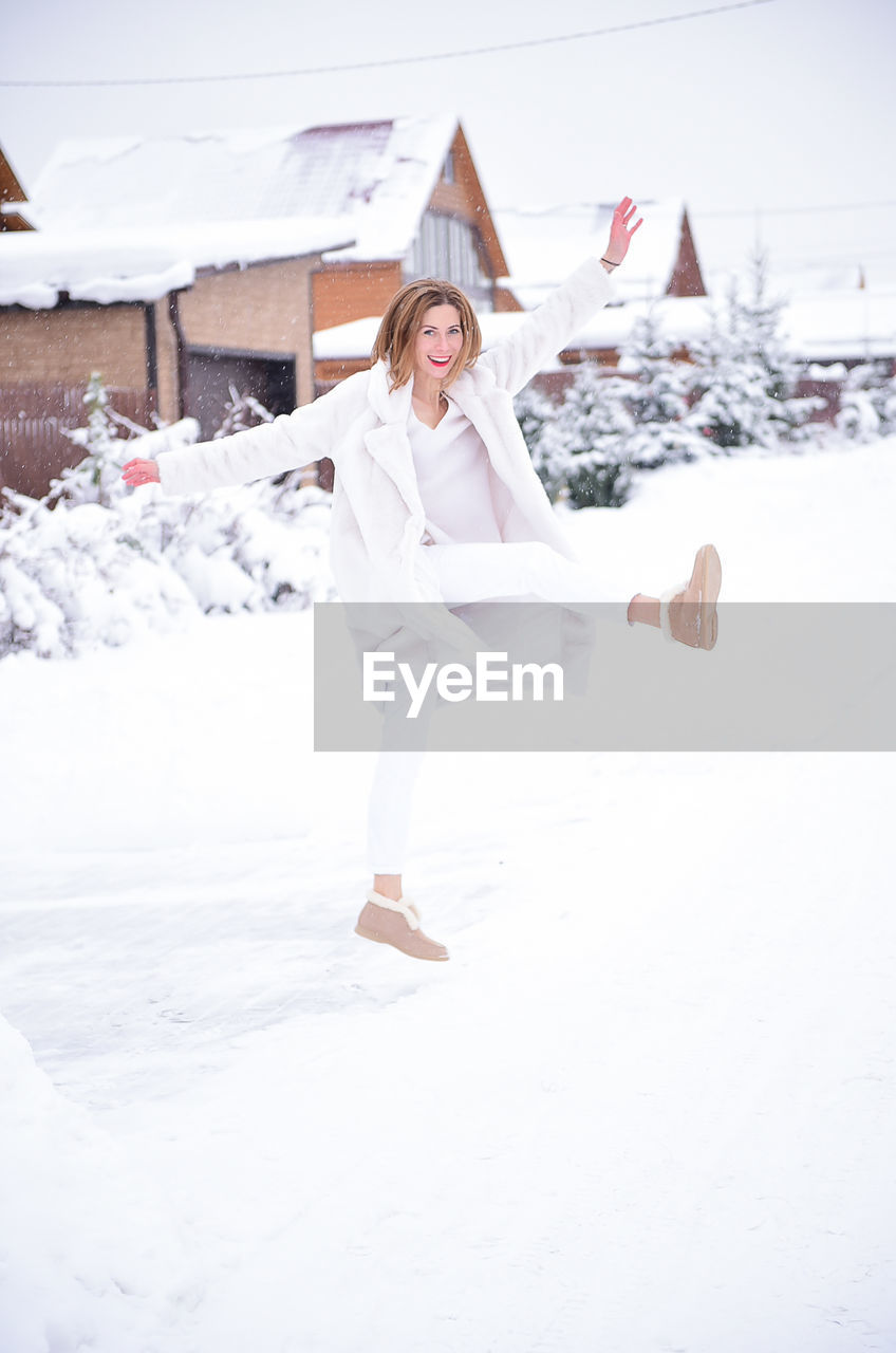 Portrait of smiling woman standing with arms outstretched on snow covered land