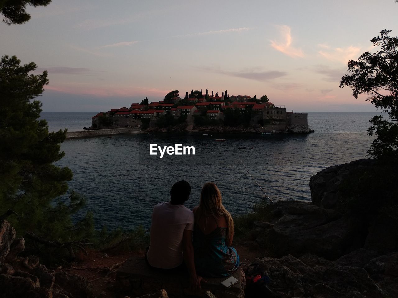 Rear view of couple sitting on rock against the sea