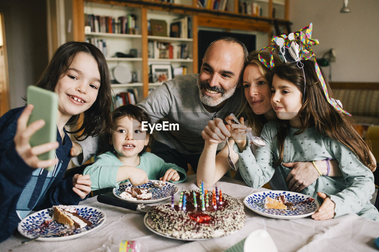 Boy taking selfie with family eating birthday cake while enjoying at home