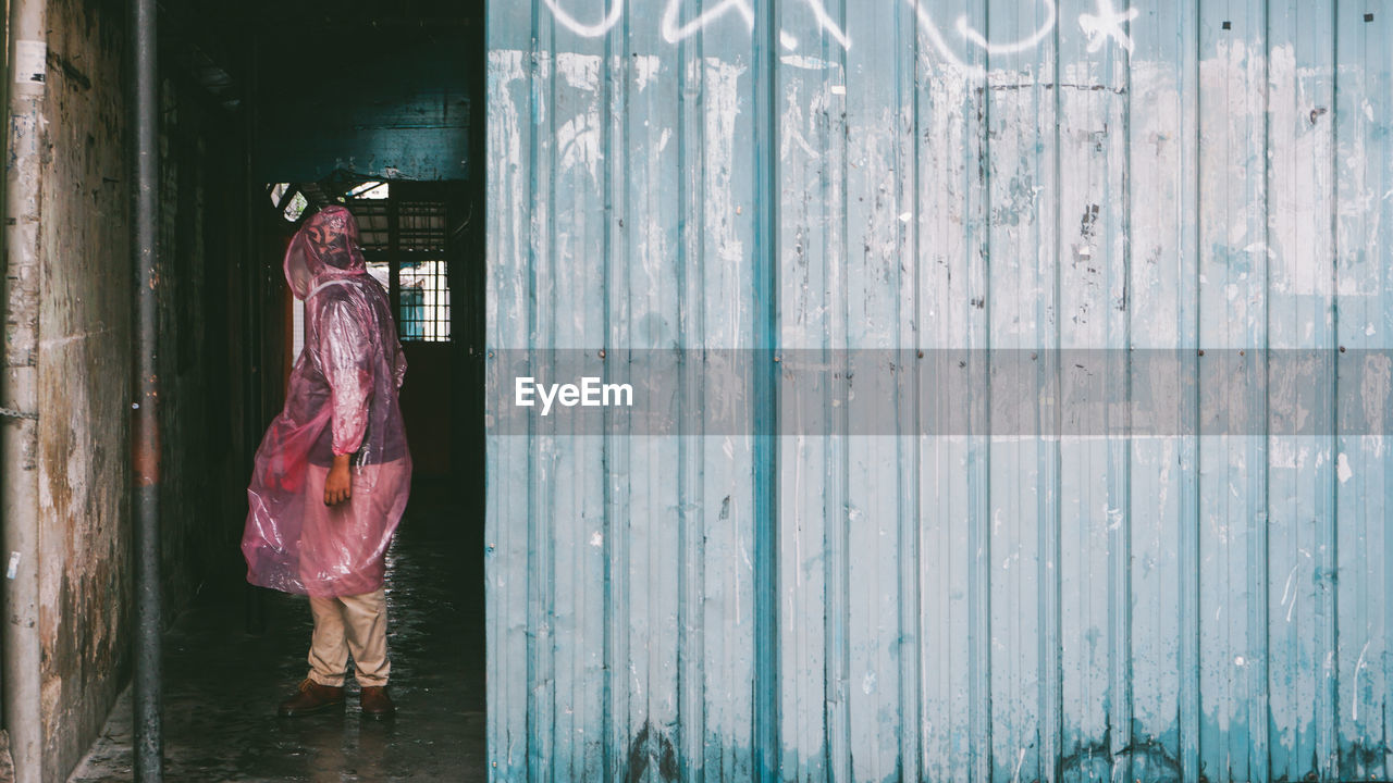 Full length of man wearing raincoat while standing by metal wall