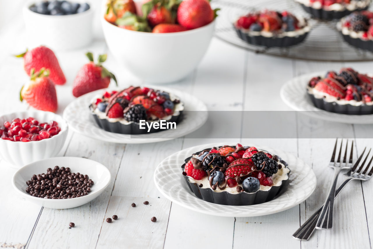 Individual homemade mixed berry cheesecake tarts on a white wooden table.