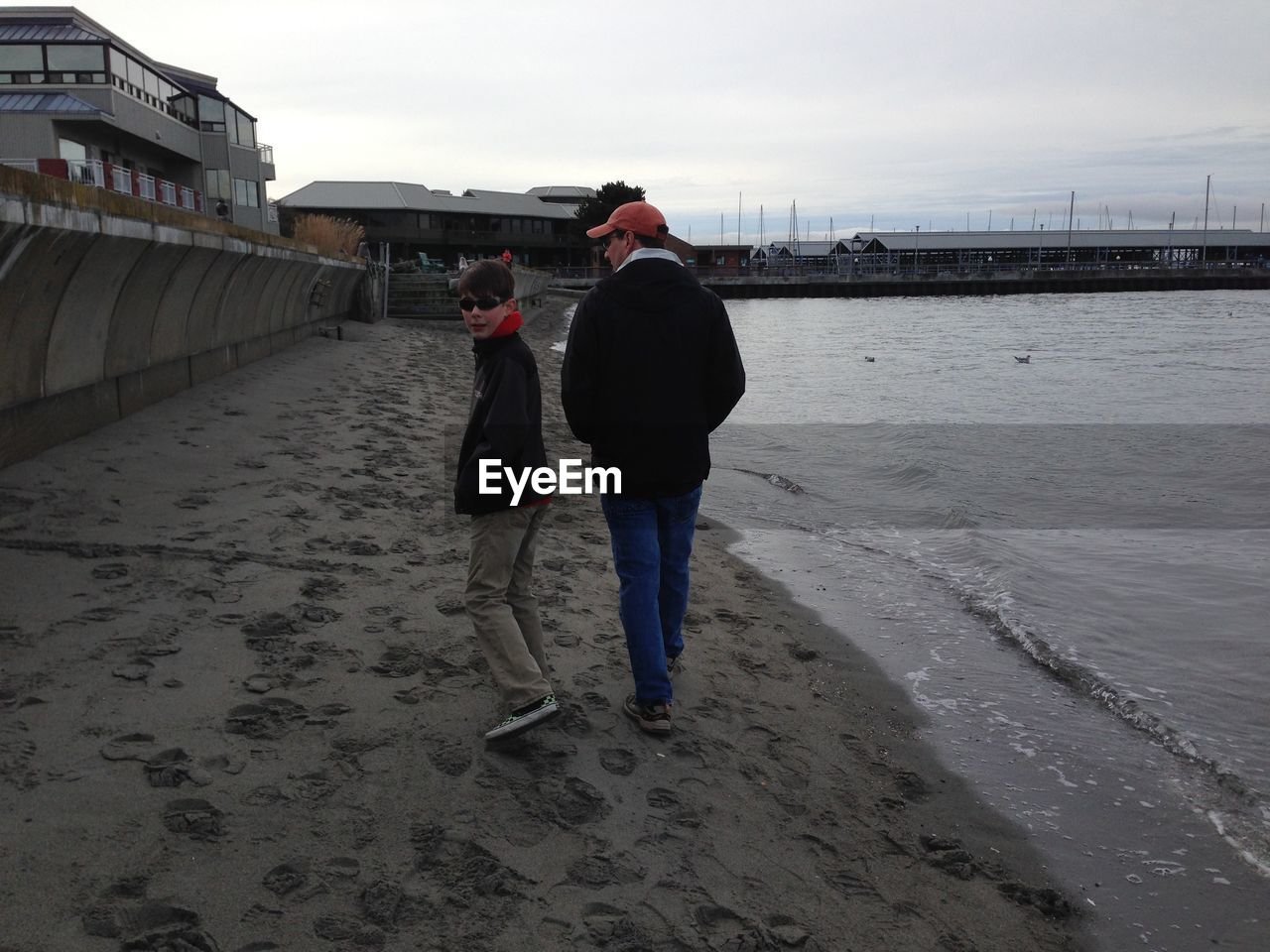 Full length rear view of man and boy walking at beach by buildings