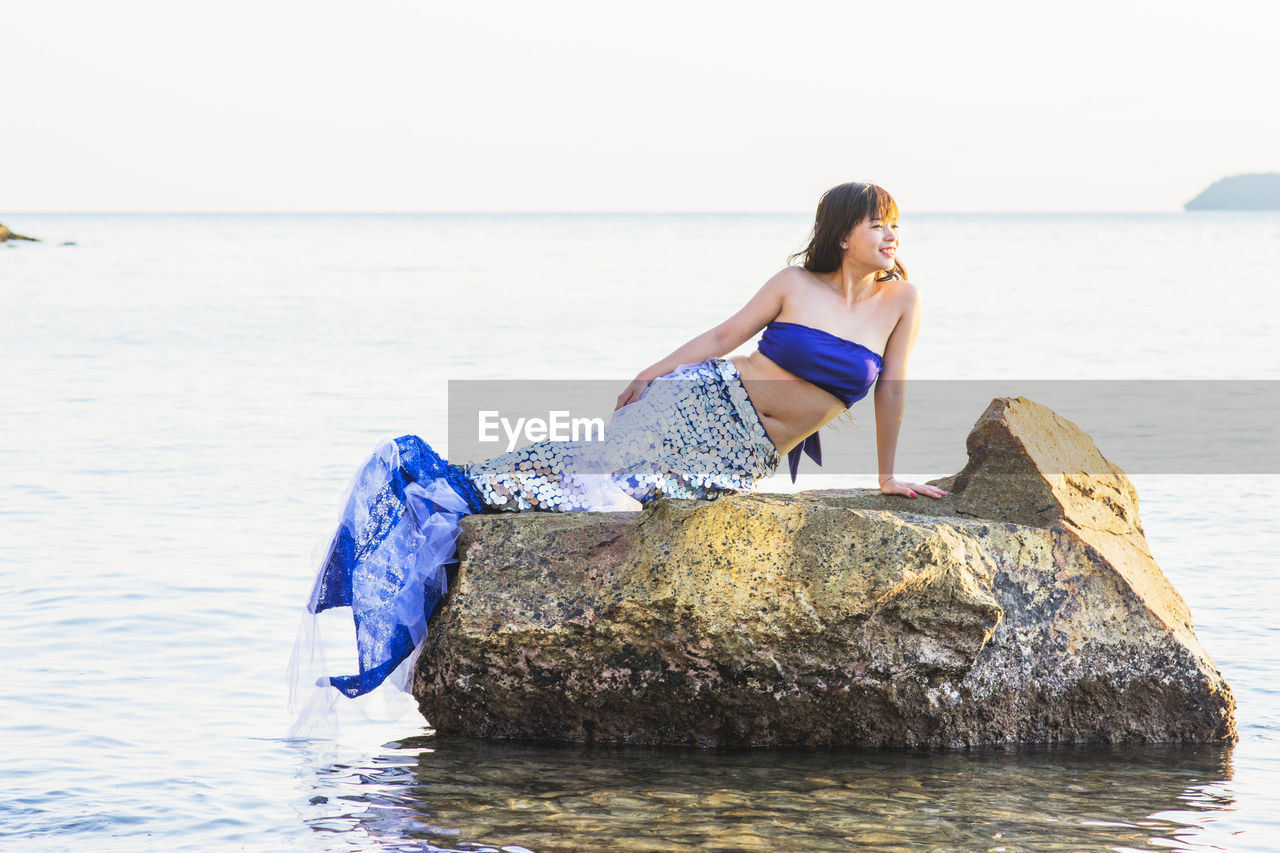 WOMAN ON ROCK AT BEACH AGAINST SKY