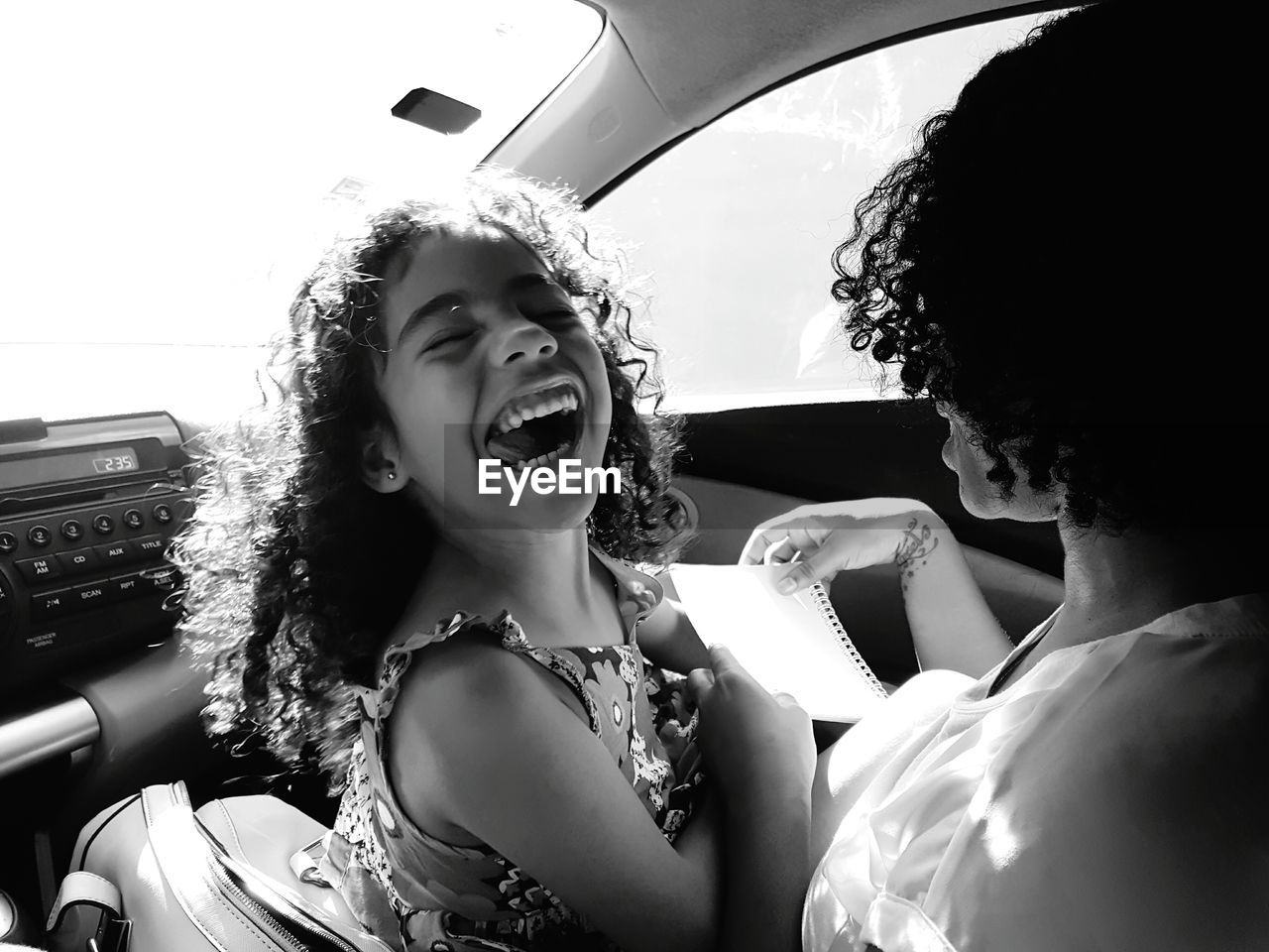 Playful daughter sticking out tongue with mother while sitting in car