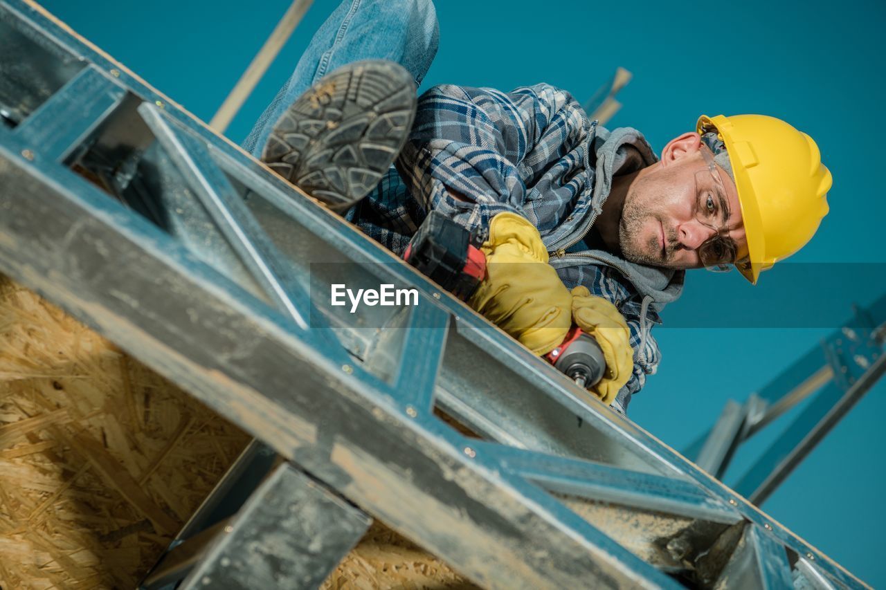 Manual worker drilling in railing against clear sky