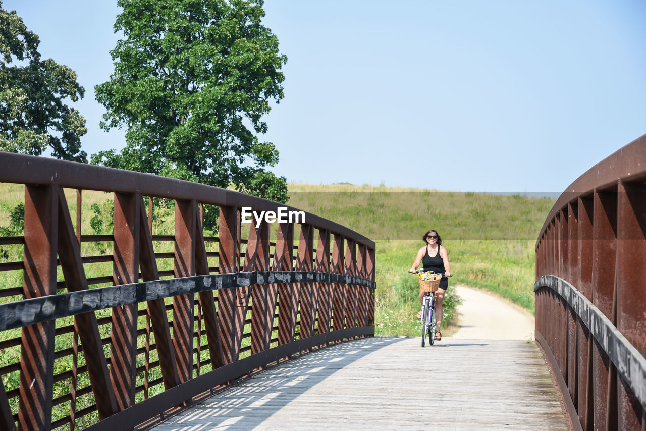 Mature woman riding bicycle on footbridge against clear sky