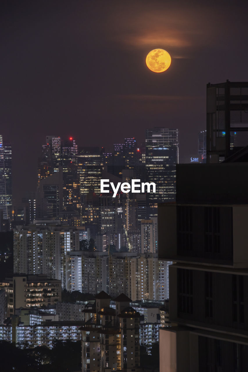Illuminated buildings in city against sky at night full moon