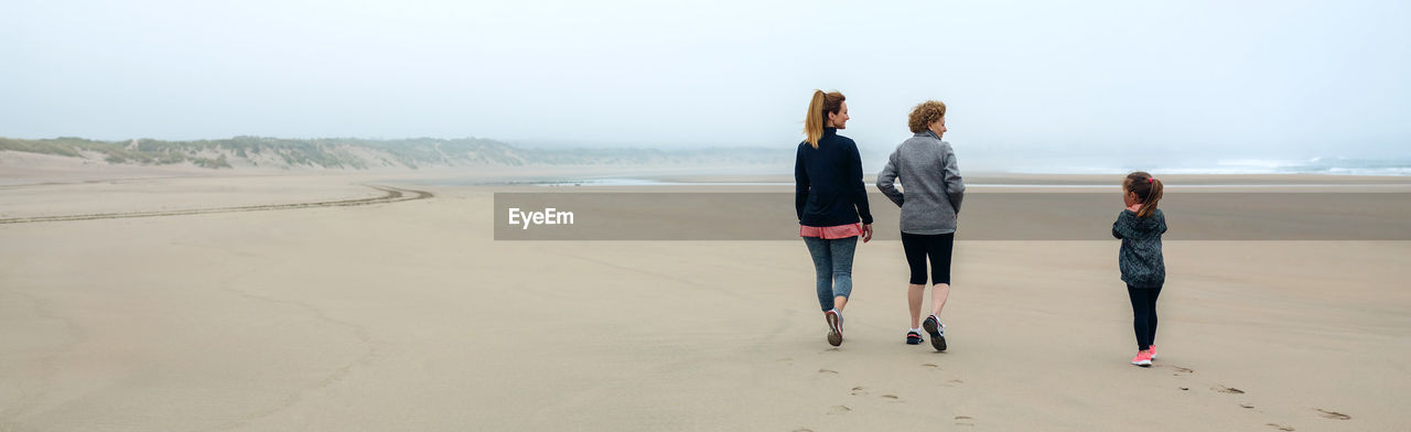 Panoramic view of people walking at beach against sky