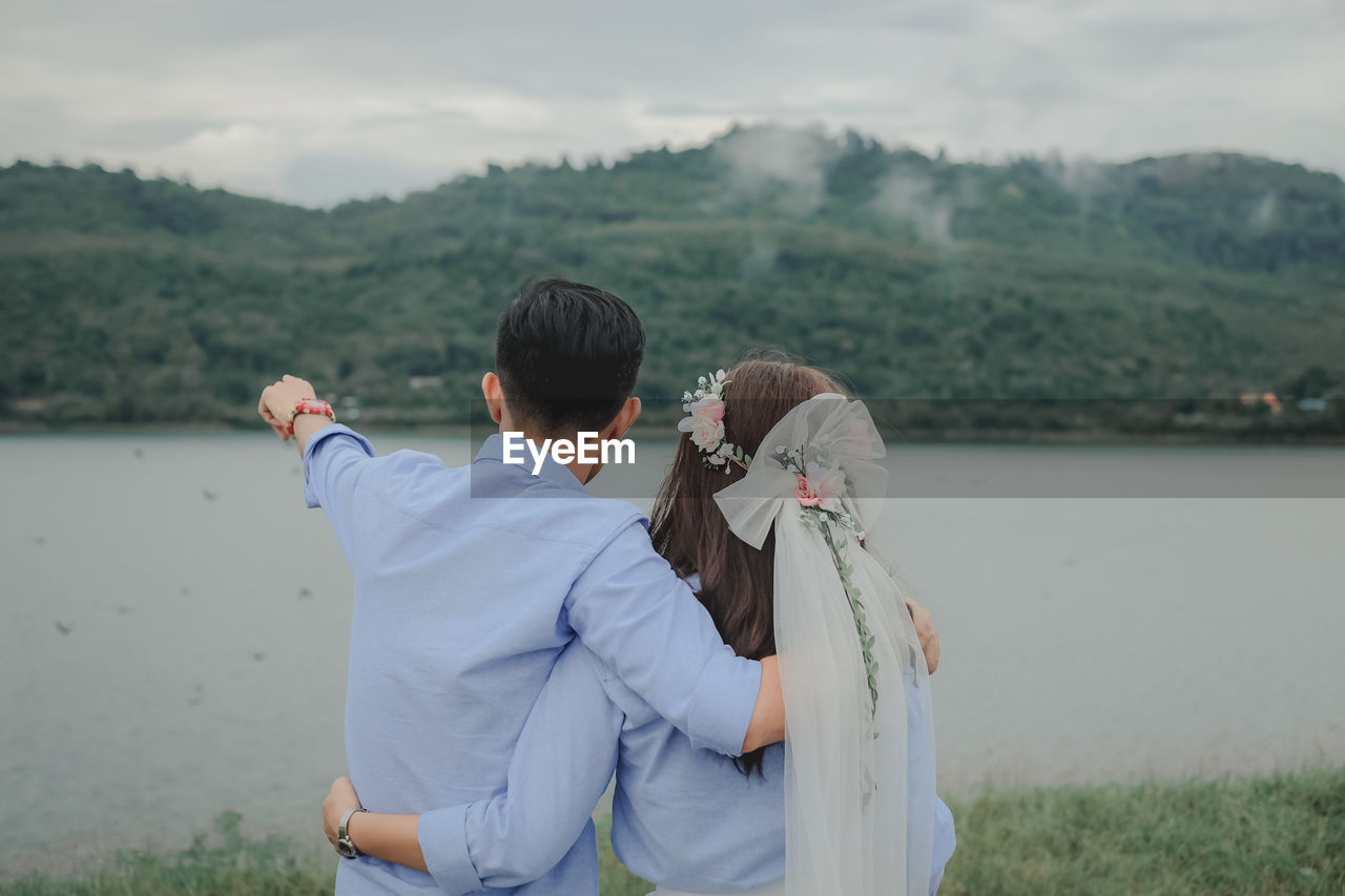 Rear view of couple standing by river against sky