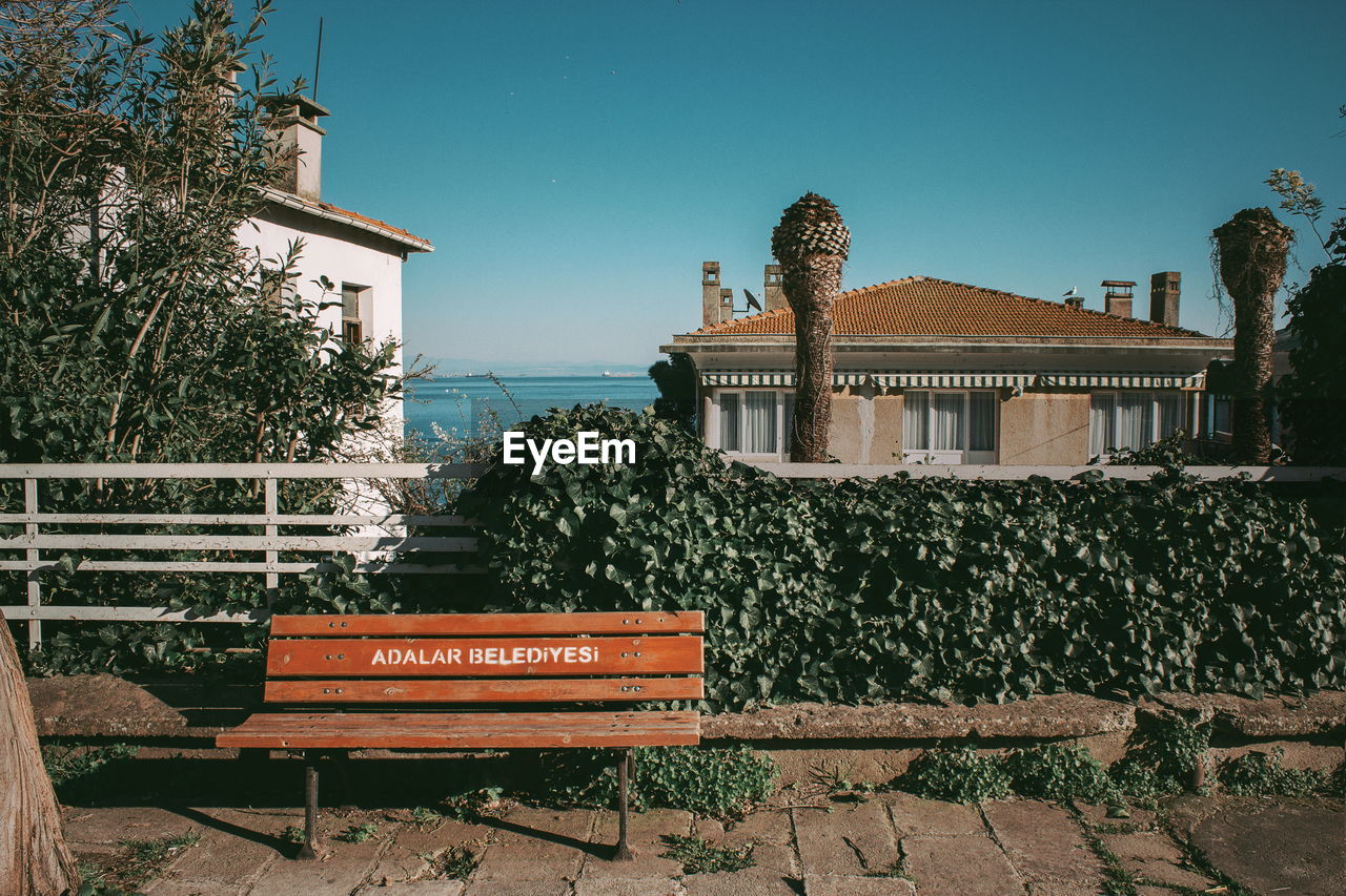 BENCH AGAINST BUILDING AND SEA AGAINST CLEAR SKY