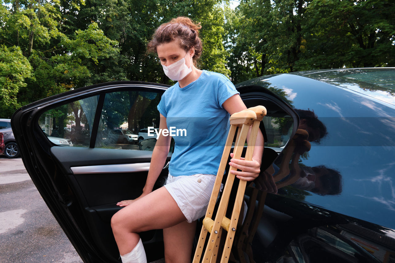 A woman with an injured leg gets into a car. orthopedic plaster, orthopedic crutches