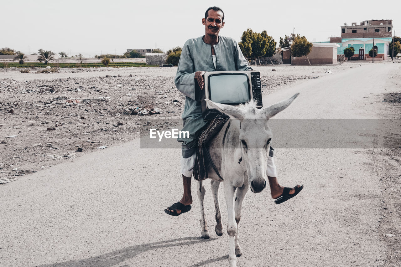 Man holding television set while sitting on donkey