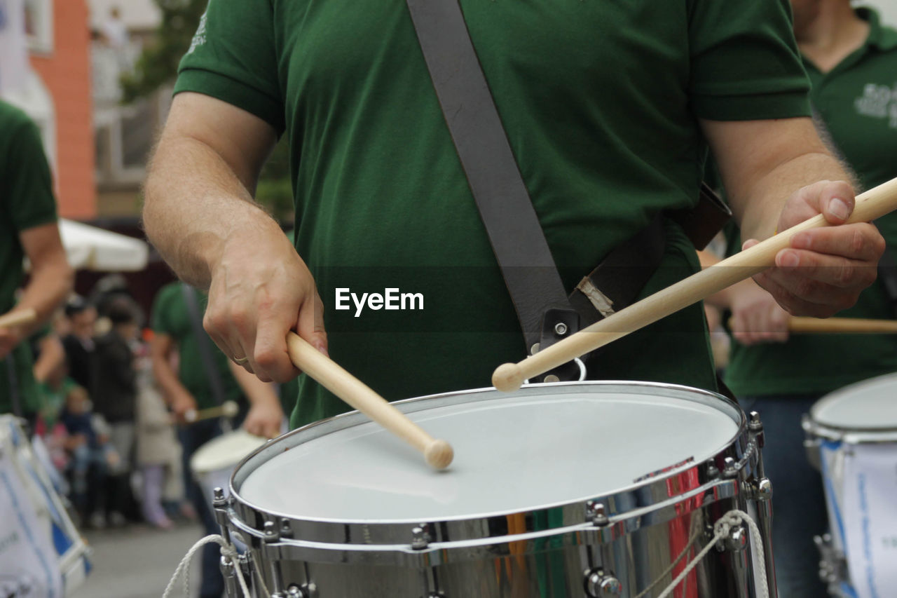 Midsection of man playing drum in city during event