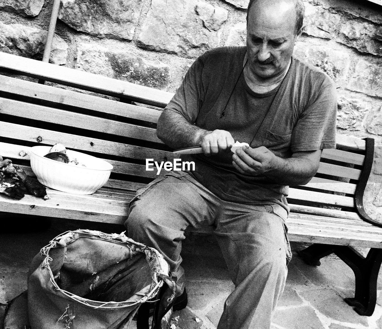 Tilt shot of man peeling mushrooms while sitting on bench