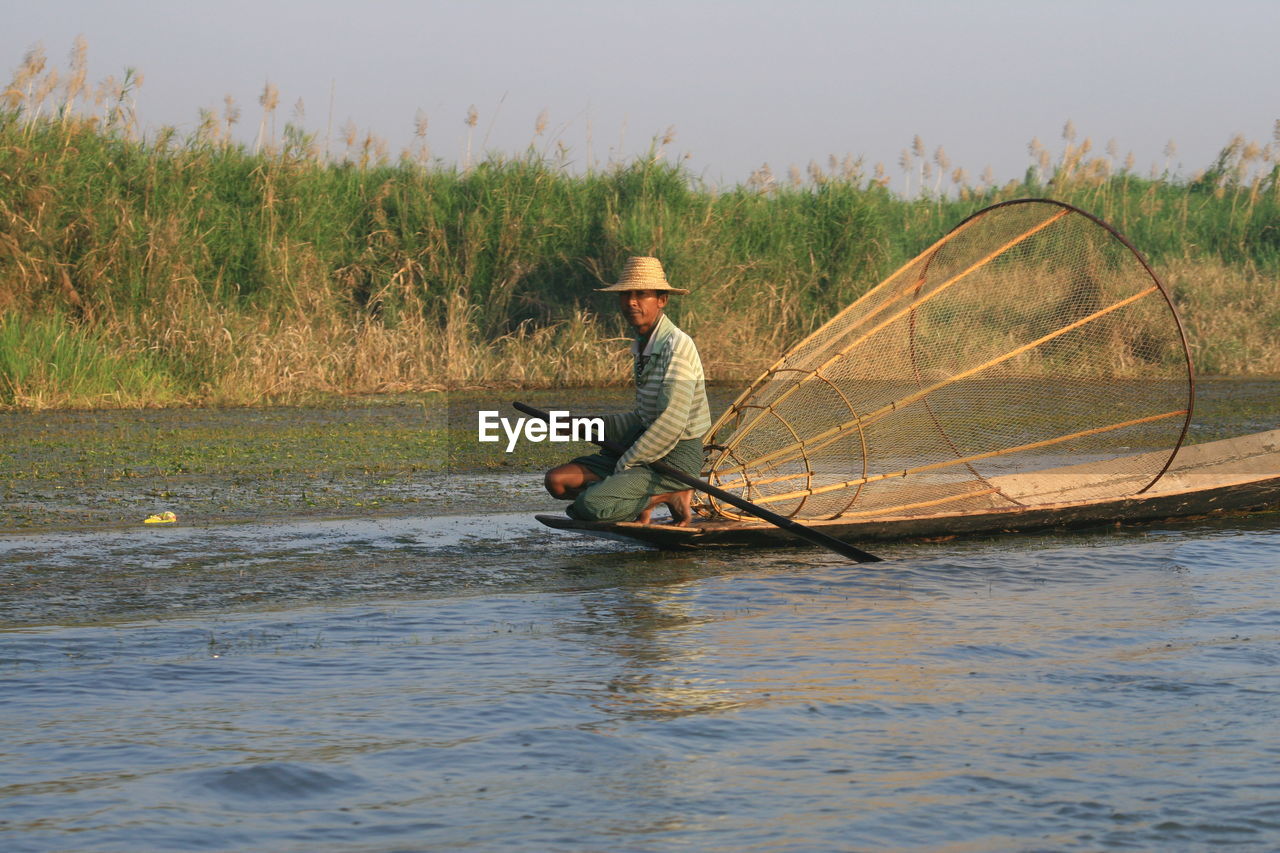 Side view of fisherman crouching on fishing boat in river