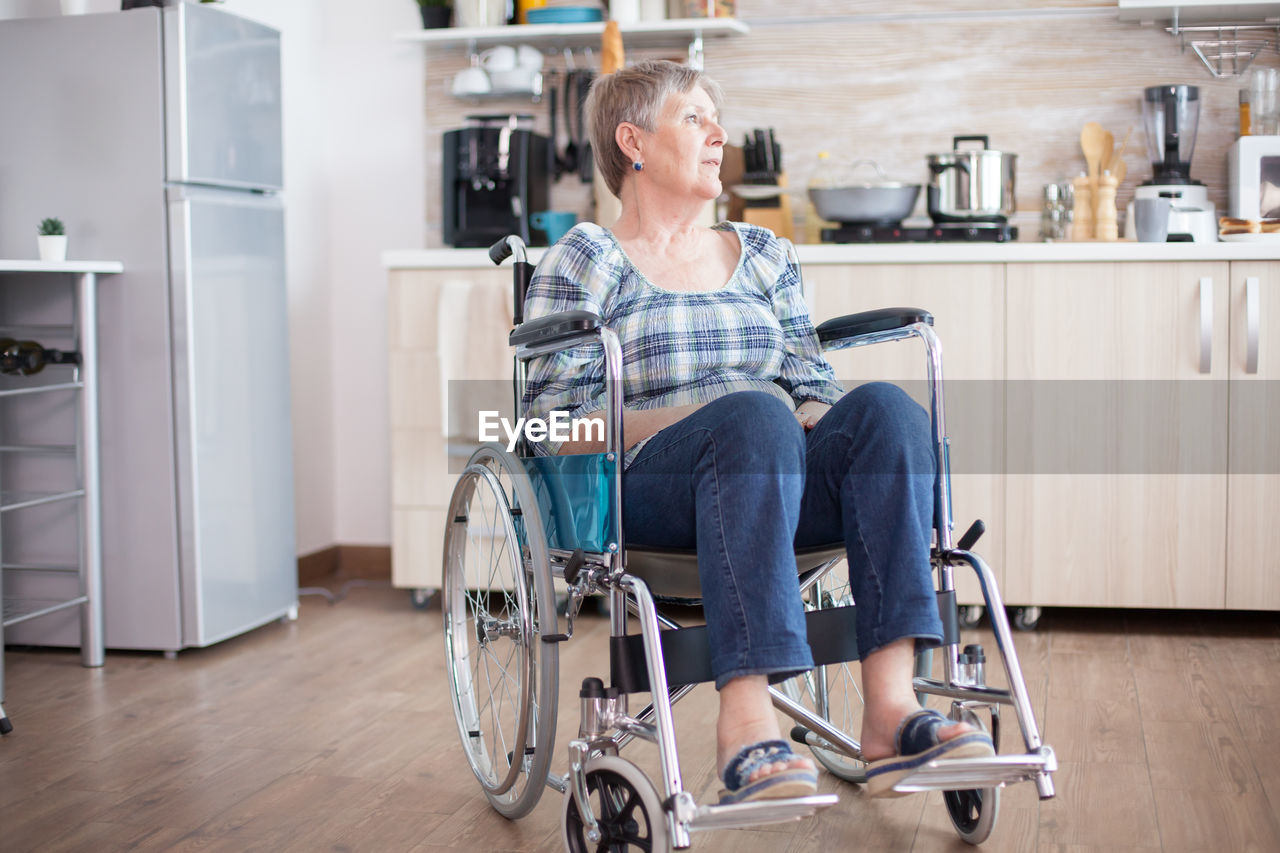 Full length of woman sitting on wheelchair at kitchen