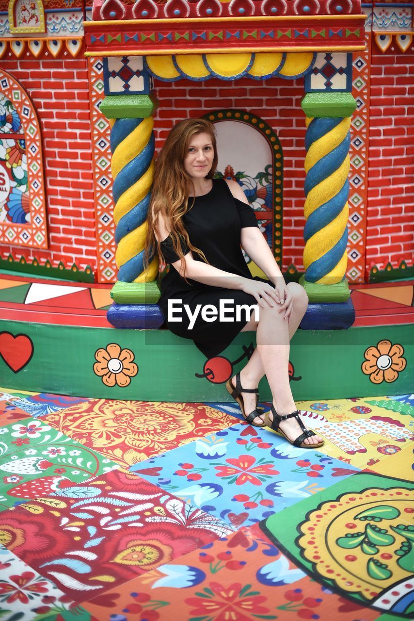 PORTRAIT OF YOUNG WOMAN SITTING ON MULTI COLORED UMBRELLAS