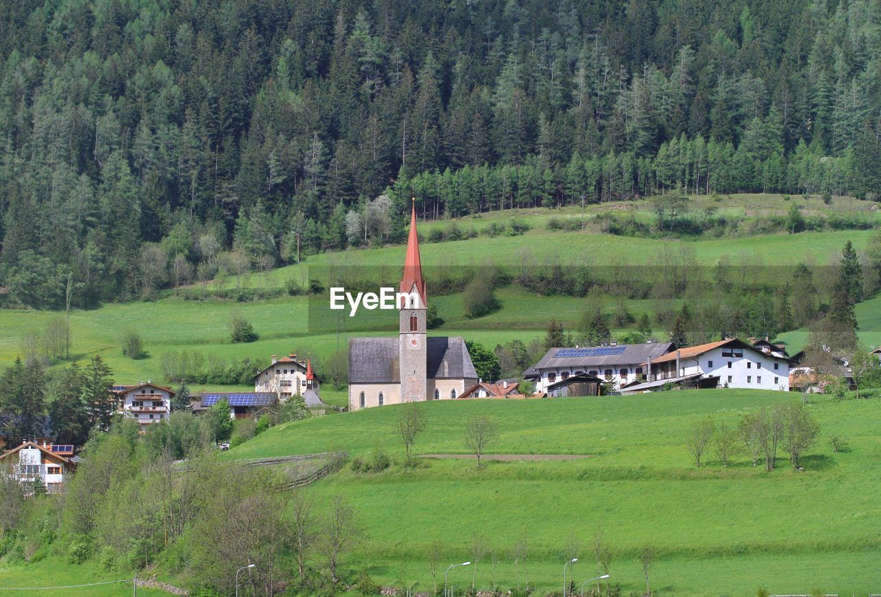 BUILT STRUCTURE ON FIELD BY TREES AND HOUSES AGAINST MOUNTAIN